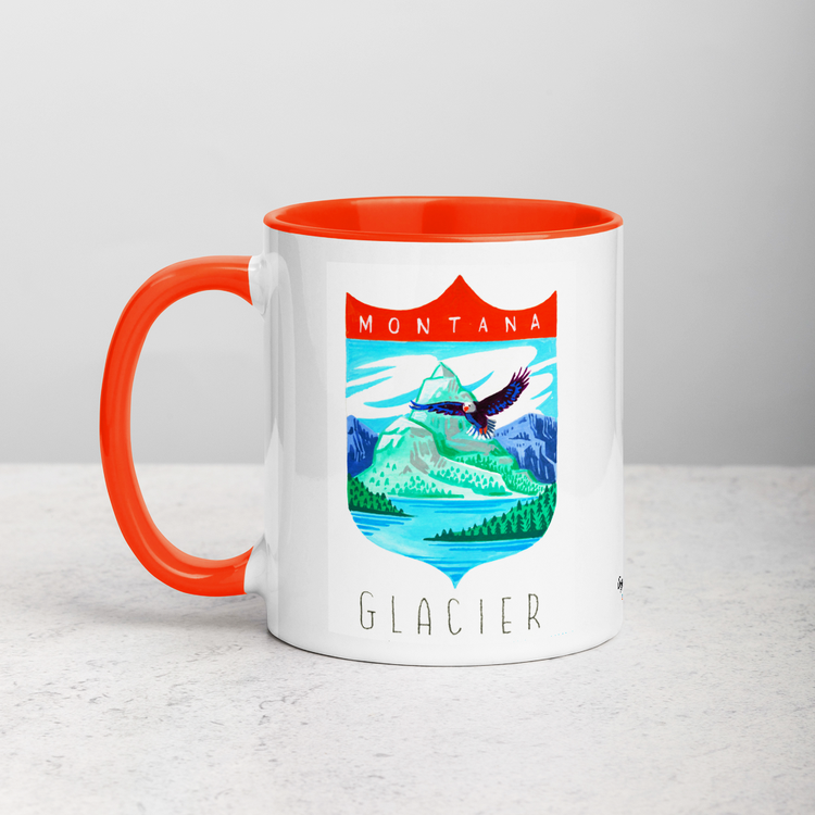 White ceramic coffee mug with orange handle and inside; has Glacier National Park illustration by Angela Staehling