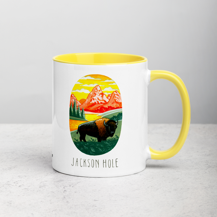 White ceramic coffee mug with yellow handle and inside; has Jackson Hole National Park illustration by Angela Staehling