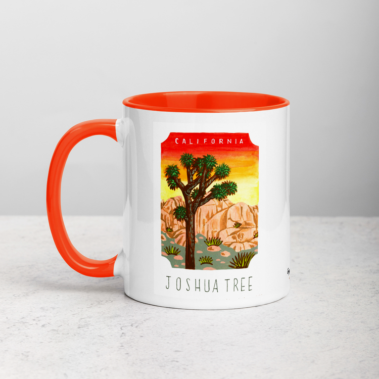 White ceramic coffee mug with orange handle and inside; has Joshua Tree National Park illustration by Angela Staehling