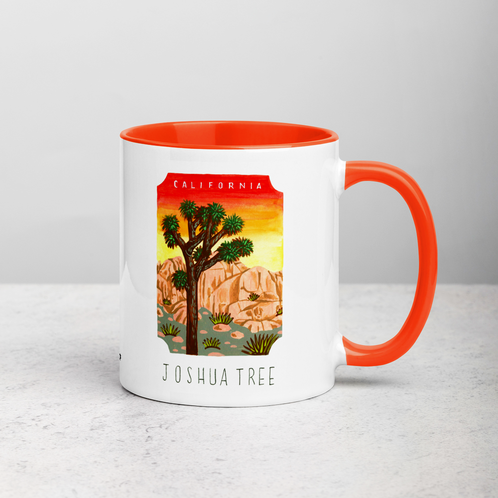 White ceramic coffee mug with orange handle and inside; has Joshua Tree National Park illustration by Angela Staehling