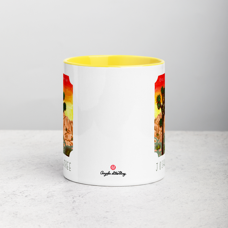White ceramic coffee mug with yellow handle and inside; has Joshua Tree National Park illustration by Angela Staehling