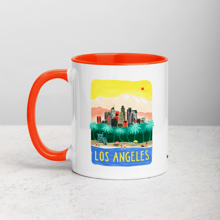 White ceramic coffee mug with orange handle and inside; has Los Angeles California illustration by Angela Staehling