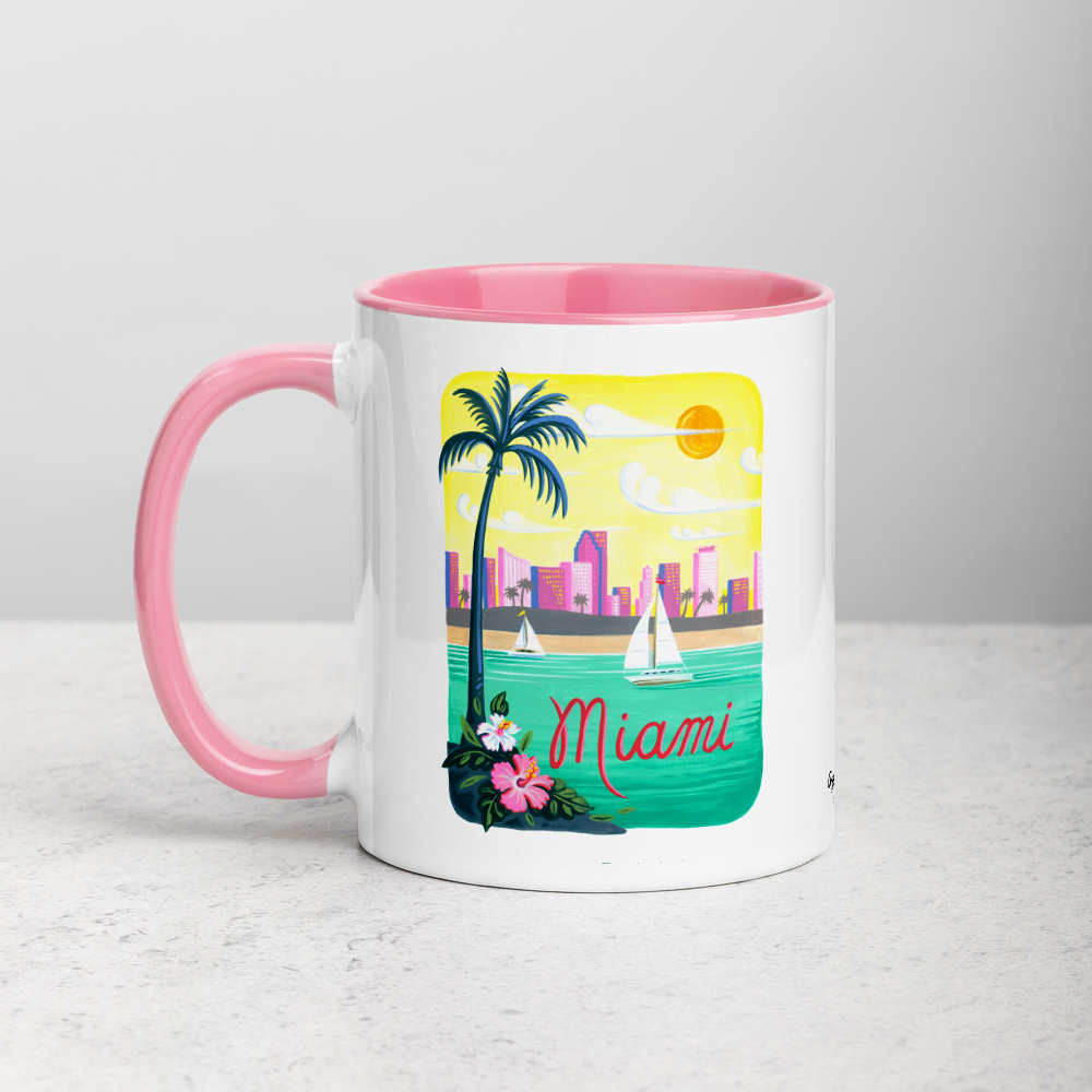 White ceramic coffee mug with pink handle and inside; has Miami Florida illustration by Angela Staehling