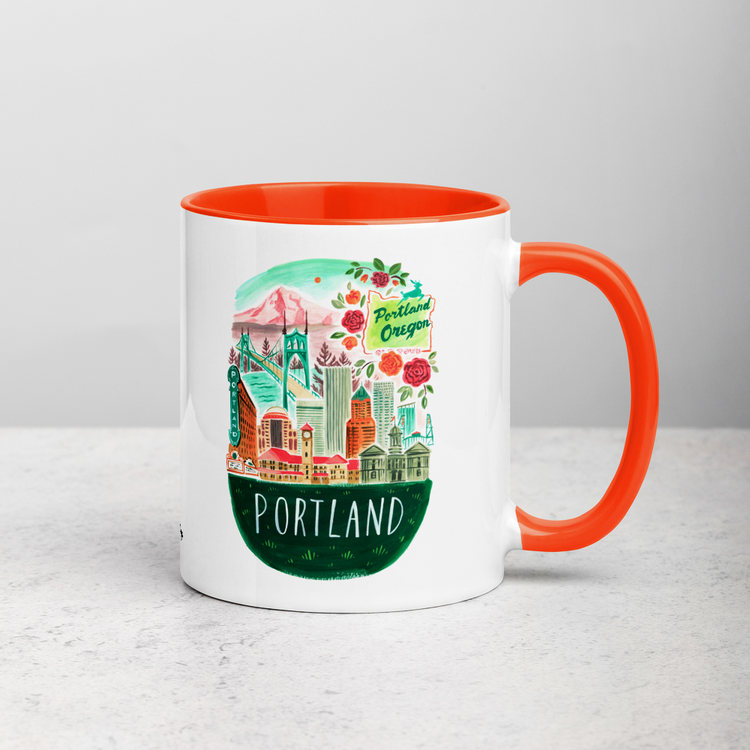 White ceramic coffee mug with orange handle and inside; has Portland Oregon illustration by Angela Staehling