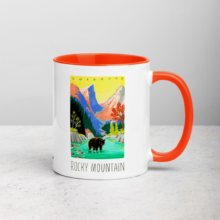 White ceramic coffee mug with orange handle and inside; has Rocky Mountain National Park illustration by Angela Staehling