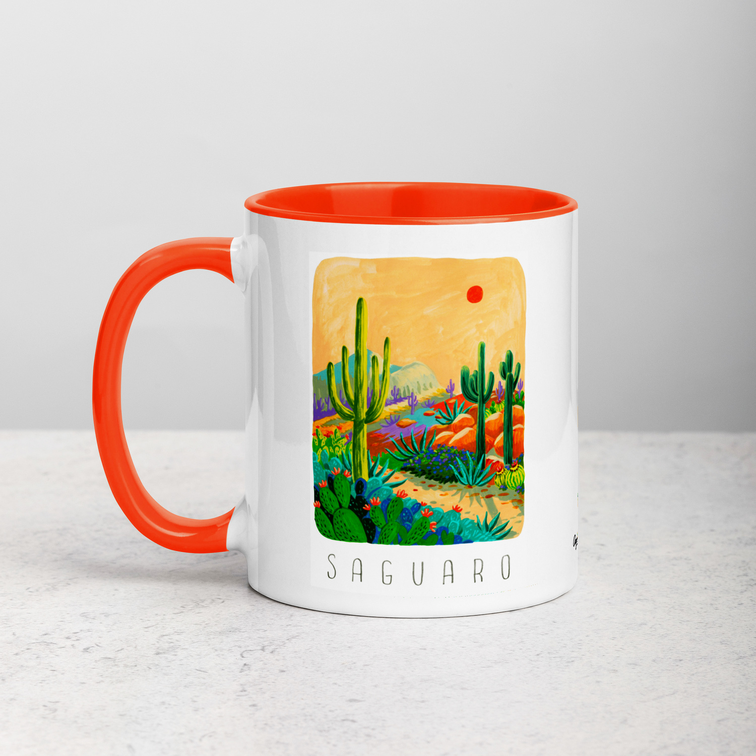 White ceramic coffee mug with orange handle and inside; has Saguaro National Park illustration by Angela Staehling