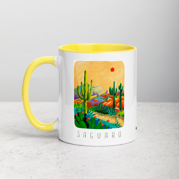 White ceramic coffee mug with yellow handle and inside; has Saguaro National Park illustration by Angela Staehling