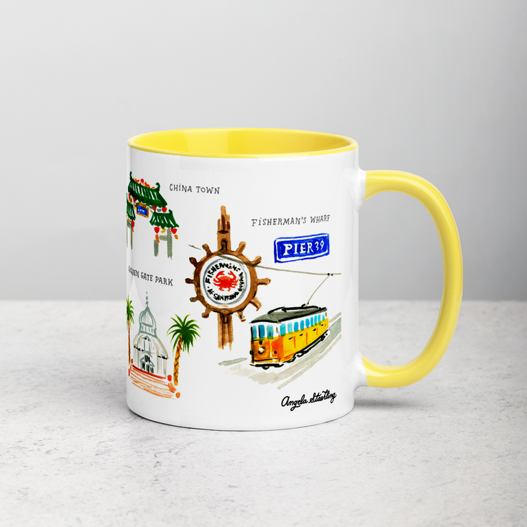 White ceramic coffee mug with yellow handle and inside; has San Francisco landmarks illustration by Angela Staehling