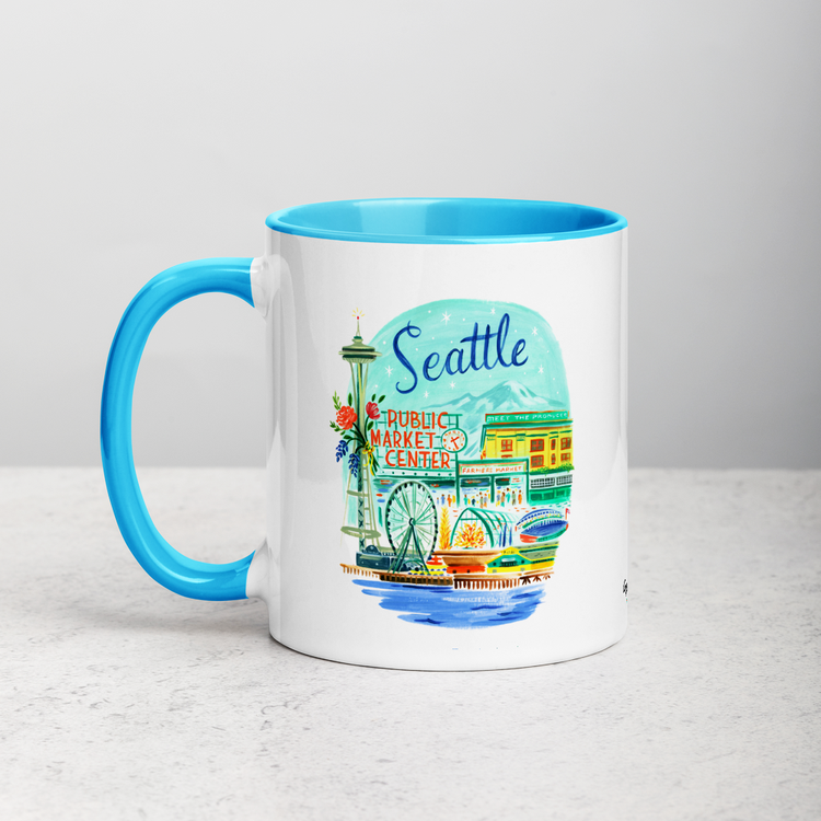 White ceramic coffee mug with blue handle and inside; has Seattle Washington illustration by Angela Staehling