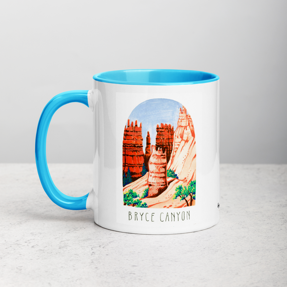White ceramic coffee mug with blue handle and inside; has Bryce Canyon art by Angela Staehling