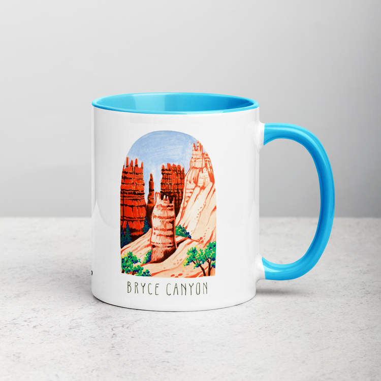 White ceramic coffee mug with blue handle and inside; has Bryce Canyon art by Angela Staehling