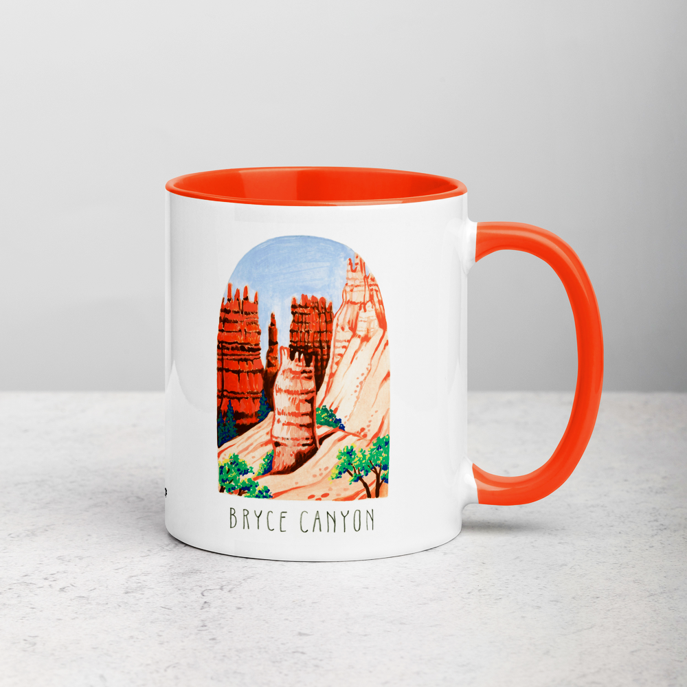 White ceramic coffee mug with orange handle and inside; has Bryce Canyon art by Angela Staehling